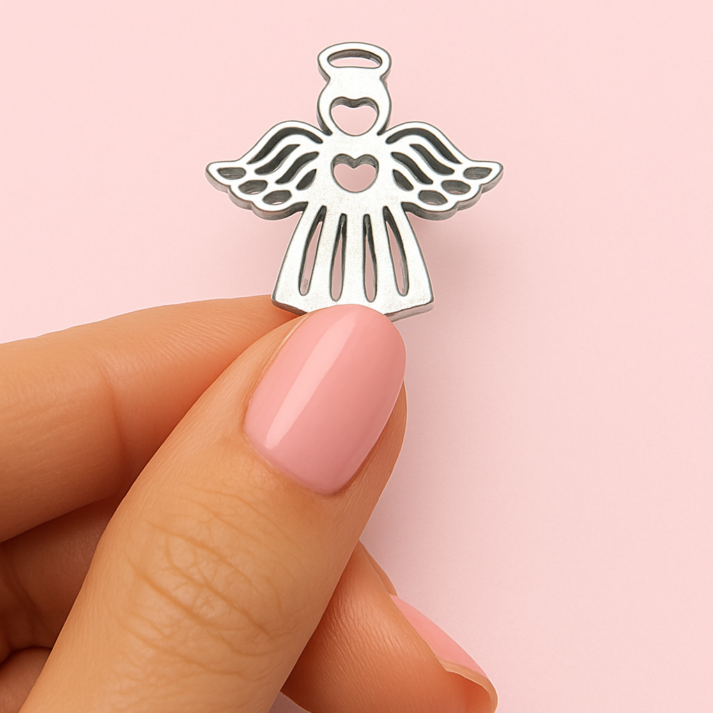 A hand holding a small silver angel charm against a pink background.