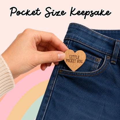 A hand holding a wooden heart-shaped keepsake attached to the pocket of a pair of blue jeans.
