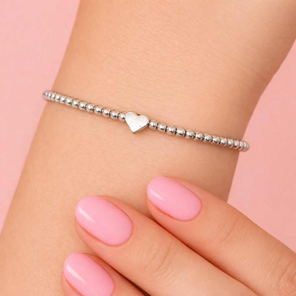 A close-up of a person's wrist wearing a silver heart-shaped charm bracelet against a pink background.